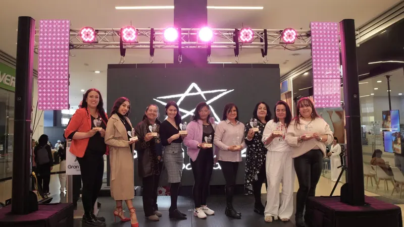 Grupo de mujeres recibiendo reconocimientos en una tarima con luces magenta