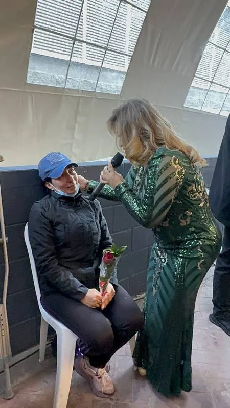 Cantante con vestido de lentejuelas verdes cantándole a una mamá del público