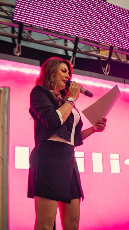 Presentadora con micrófono frente a la pantalla rosada