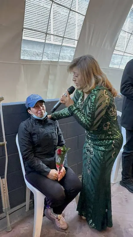 Cantante con vestido de lentejuelas verdes cantándole a una mamá con una rosa