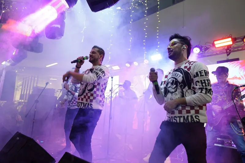 Cantantes con suéteres navideños en tarima entre humo y luces moradas